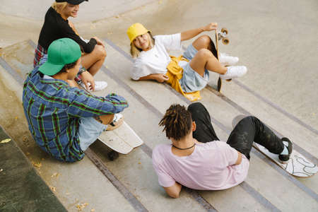 Multiracial friends smiling and talking while resting in skate park on summer dayの写真素材