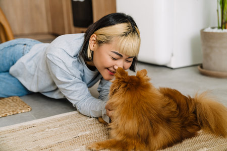 Asian girl playing with her ginger dog while lying on floor at home