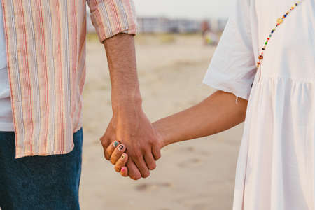 Multiracial couple holding hands while walking on summer beach