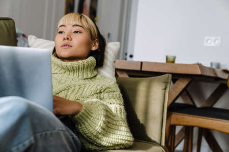 Asian girl working with laptop while resting on sofa at home