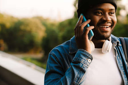 Black man with headphones talking on mobile phone while walking in autumn parkの写真素材