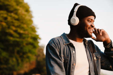 Black young man listening music with headphones while walking in parkの写真素材