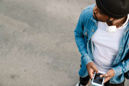 Black man with headphones using mobile phone while standing outdoorsの写真素材
