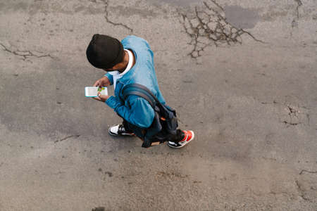 Black man with headphones using mobile phone while walking outdoorsの写真素材