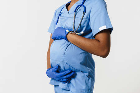 Black pregnant doctor wearing face mask posing with stethoscope isolated over white background