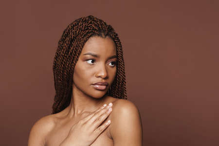 Half-naked black woman posing and looking aside isolated over brown background