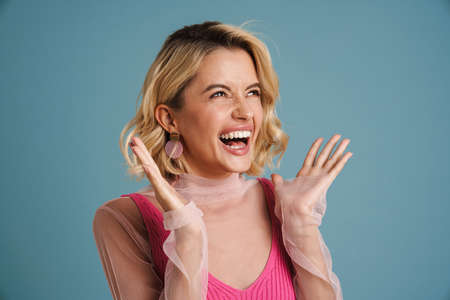Young white woman with blonde hair laughing and gesturing isolated over blue wall