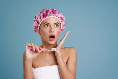 Young woman expressing surprise while brushing her teeth isolated over blue wall