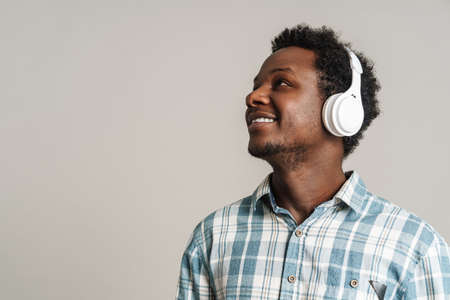 Black man smiling while listening music with headphones isolated over white backgroundの写真素材