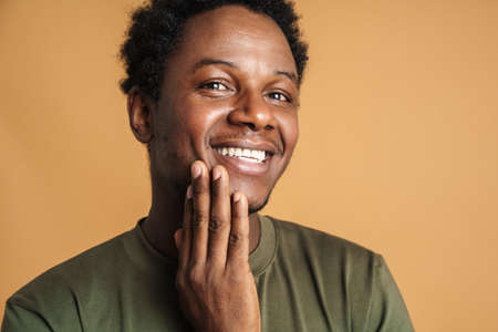 Young black man wearing t-shirt smiling and looking at camera isolated over beige backgroundの写真素材