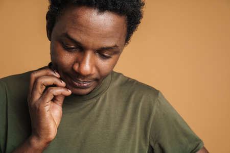 Young black man wearing t-shirt posing and looking downward isolated over beige background