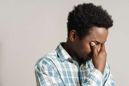Black unshaven man in plaid shirt posing while covering her eyes isolated over white backgroundの写真素材