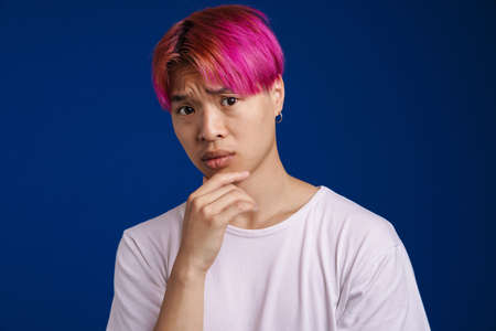 Asian boy with pink hair frowning and looking at camera isolated over blue backgroundの写真素材