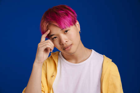 Asian boy with pink hair smiling and looking at camera isolated over blue backgroundの写真素材