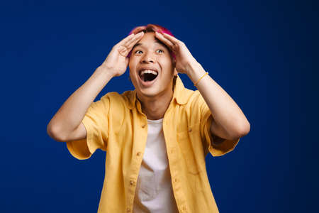 Asian boy expressing surprise while covering her face isolated over blue background