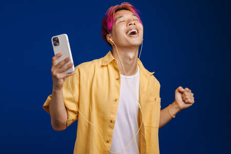 Asian boy with pink hair listening music and dancing isolated over blue backgroundの写真素材