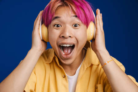 Asian boy with pink hair listening music and singing isolated over blue backgroundの写真素材