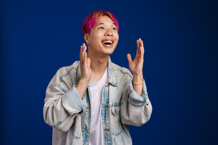 Asian boy with pink hair expressing surprise at camera isolated over blue backgroundの写真素材