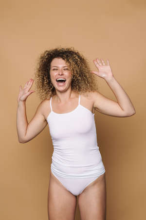 Young blonde woman wearing underwear making fun on camera isolated over beige backgroundの写真素材