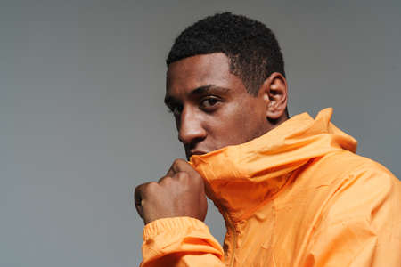Young black man dressed in sports jacket posing and looking at camera isolated over grey wall
