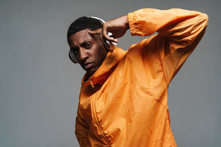 Young black man in wireless headphones pointing finger at his temple isolated over grey wall