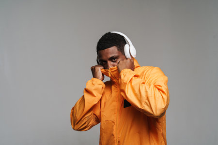 Young black man listening music with wireless headphones isolated over grey wall