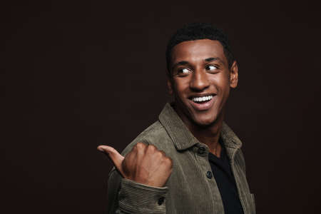 Young black man dressed in shirt smiling and pointing finger aside isolated over brown wall