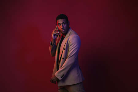 Young black man dressed in jacket talking on mobile phone isolated over red wall