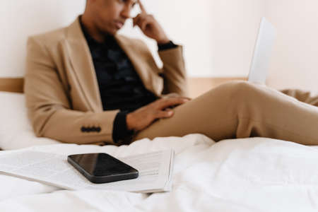Black man working on laptop while sitting on bad at hotel
