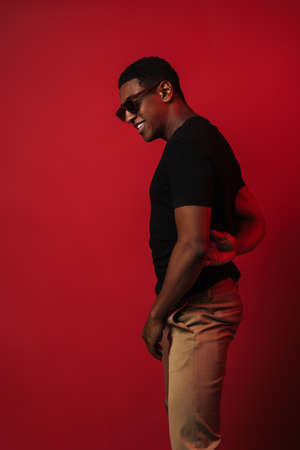 Young black man wearing sunglasses laughing and looking aside isolated over red wall