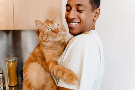Black man wearing t-shirt smiling while petting his cat in hotelの写真素材