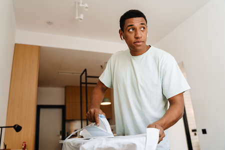 Black man listening music while ironing his shirt on board in hotelの写真素材