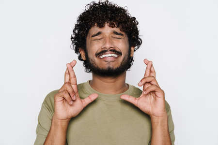 Young middle eastern man smiling while holding fingers together isolated over white wallの写真素材