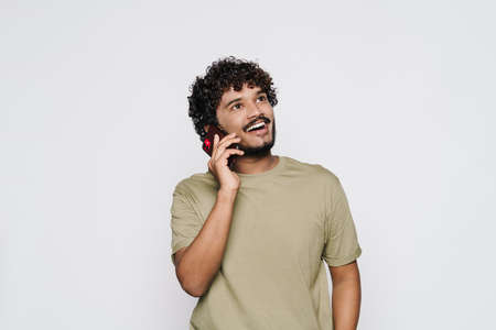 Young middle eastern man smiling while talking on cellphone isolated over white wall