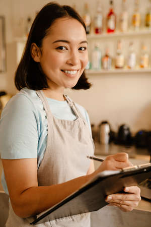 Young asian barista wearing apron smiling while working in cafe