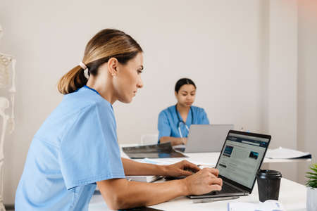 Multiracial women doctors working with laptops in office indoors