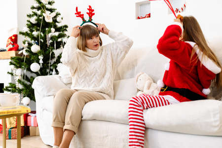 White family wearing Christmas reindeer antlers headbands while sitting on sofa at homeの写真素材