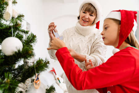 White girl decorating Christmas tree with her grandmother at home