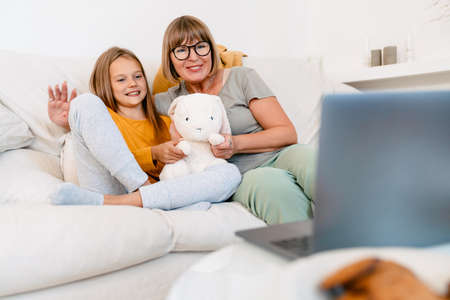 White girl and her grandmother playing with toy while using laptop on sofa at home