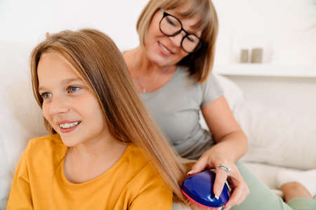 White woman combing her granddaughter's hair while sitting on sofa at home