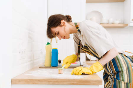 White young woman in gloves cleaning table with brush at home