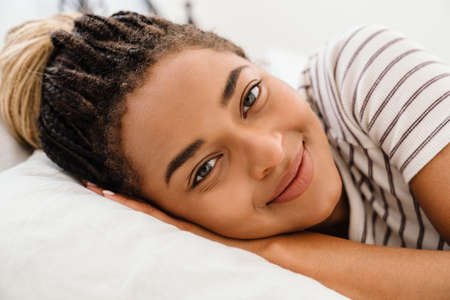 Young black woman with pigtails smiling while lying in bed at home