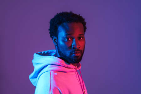 Young black man in hoodie posing and looking at camera isolated over purple wallの写真素材