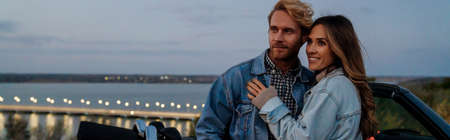 White mid couple smiling and hugging while standing by car during tripの写真素材