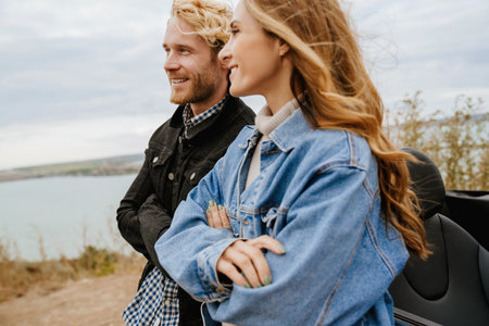 White mid couple smiling together while standing by car during trip