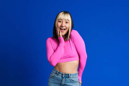 Asian girl with multicolored hair smiling and looking at camera isolated over blue wall