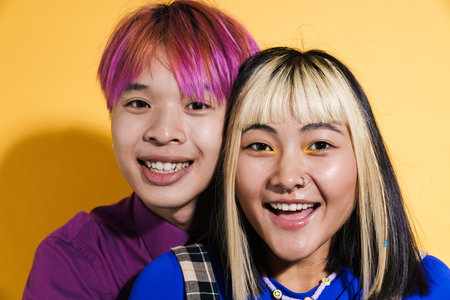 Asian couple with multicolored hair hugging and laughing together isolated over yellow wallの写真素材