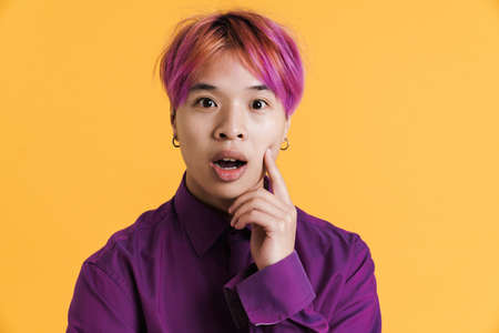 Asian boy with pink hair expressing surprise at camera isolated over yellow wall