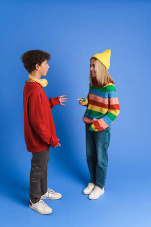 White girl and boy smiling and gesturing while talking isolated over blue background