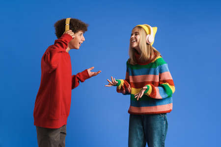 White two teenagers smiling while listening music together isolated over blue wall